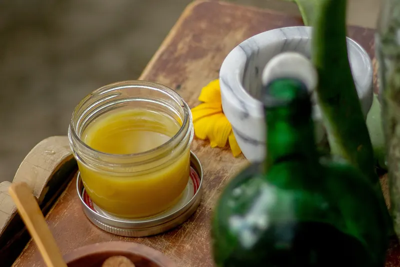 Ghee, Kräutersalben und ein Mörser auf einem Holzbrett